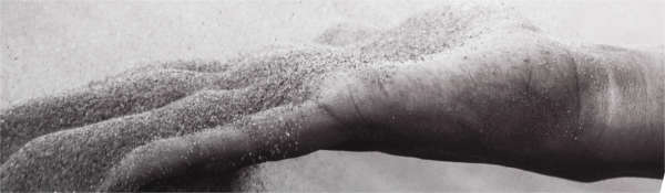 Black and white image of outstretched hand with grains of sand falling through the fingers
